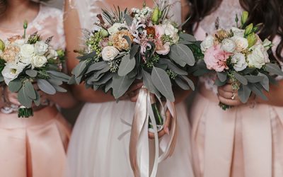 Bridesmaids and bride holding modern wedding bouquets of pink roses and green eucalyptus with pink ribbons. Stylish Contemporary bouquets on soft fabric. Wedding arrangements